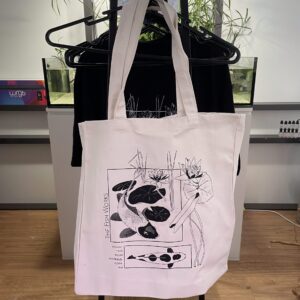 White tote bag hanging on rack with Black abstract graphic of shapes and figures on front
